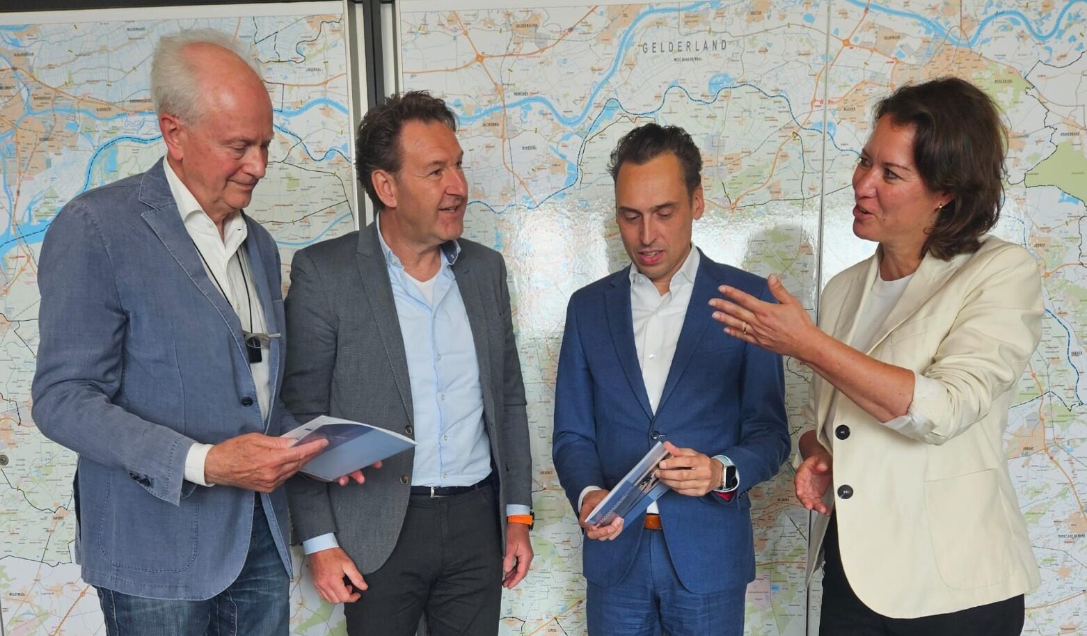 Drie mannen en een vrouw staan naast elkaar met in hun handen een nieuw rapport van Bouwend Nederland en de Fietsersbond.